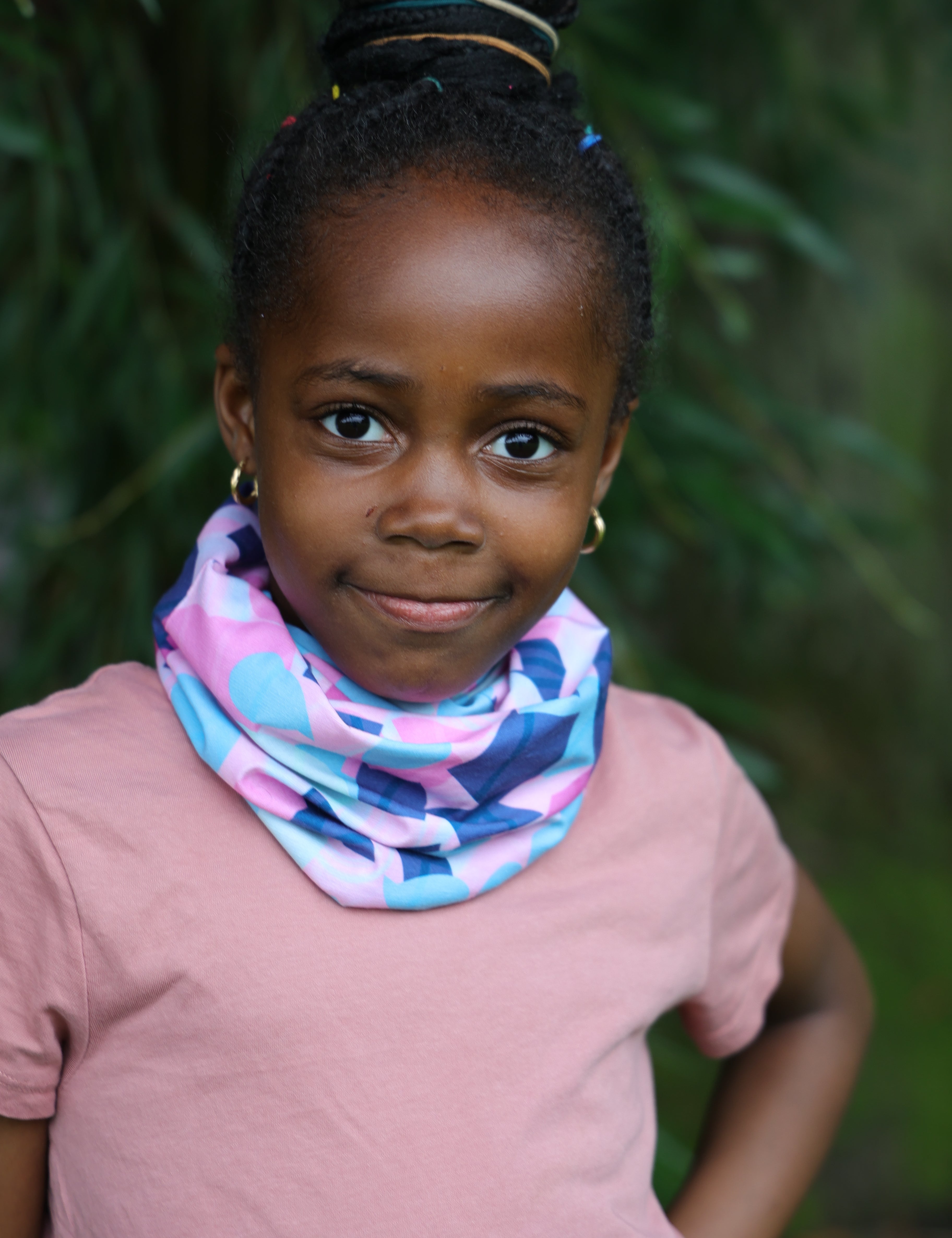 Young girl outdoors in nature wearing the pink, turquoise and navy Infinity Band (snood) around her neck with a pink t-shirt to match.